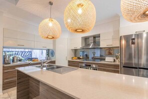 Une cuisine moderne dotée d’un îlot central, d’appareils électroménagers en acier inoxydable et de luminaires suspendus.