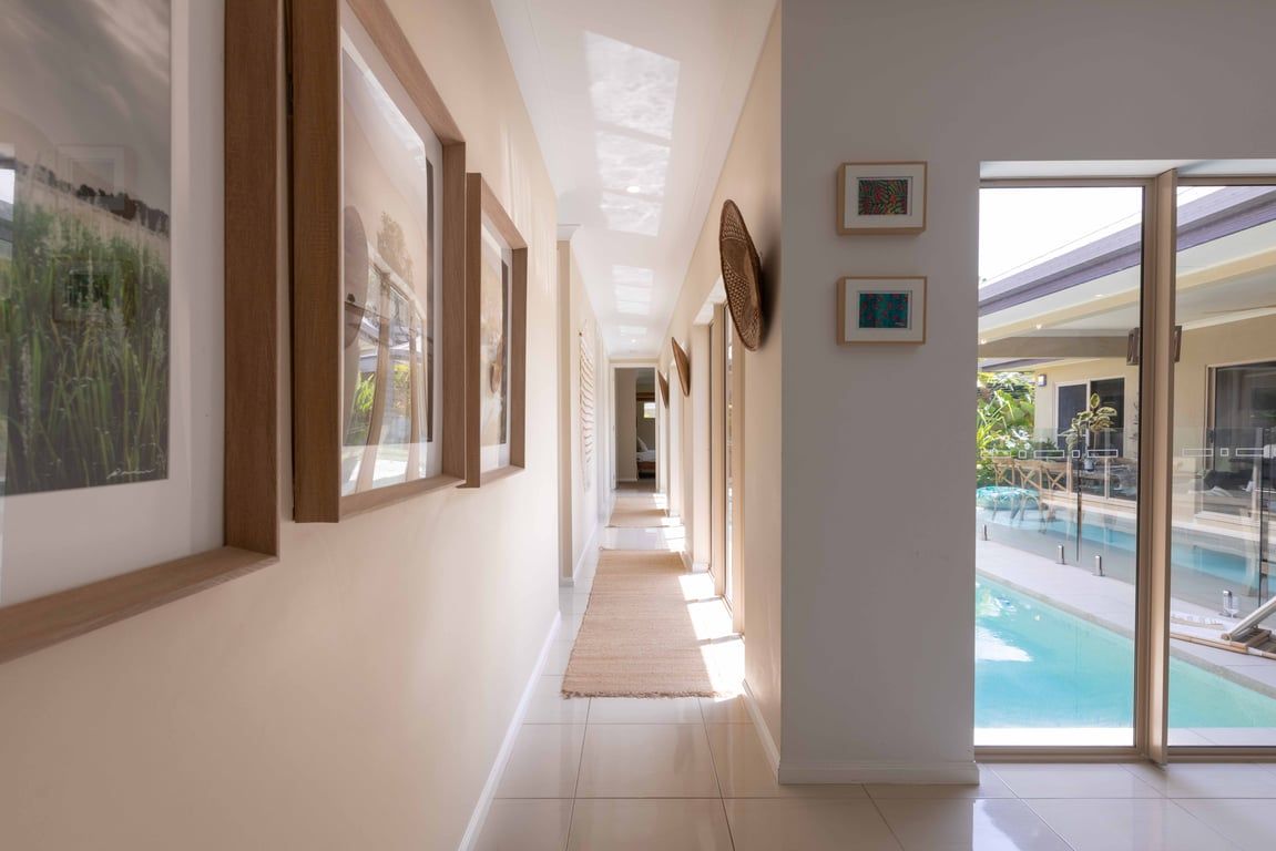 A hallway with framed artwork, a view of a pool, and a glass door leading outside.