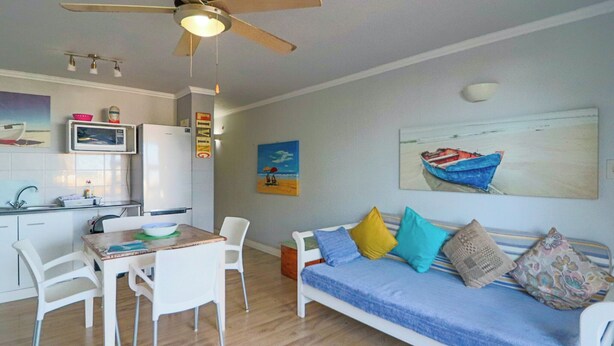 A compact living space with a dining area, kitchenette, and a sofa with cushions.