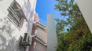 A modern building with a staircase, outdoor air conditioning units, and a view of greenery.