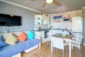Un espacio habitable compacto con kitchenette, comedor y zona de estar con sofá y sillas.