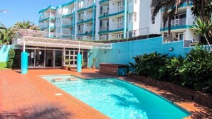 A hotel with a swimming pool, a covered entrance, and a multi-story building with balconies.