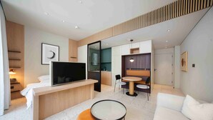 A modern hotel room with a flat-screen TV, a sofa, a round coffee table, a dining area with a small table and chairs, and a kitchenette. - Sleek Studio w/ Burj Khalifa View (Dubai)