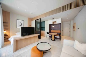 A modern hotel room with a flat-screen TV, a sofa, a round coffee table, a dining area with a small table and chairs, and a kitchenette. - Sleek Studio w/ Burj Khalifa View (Dubai)