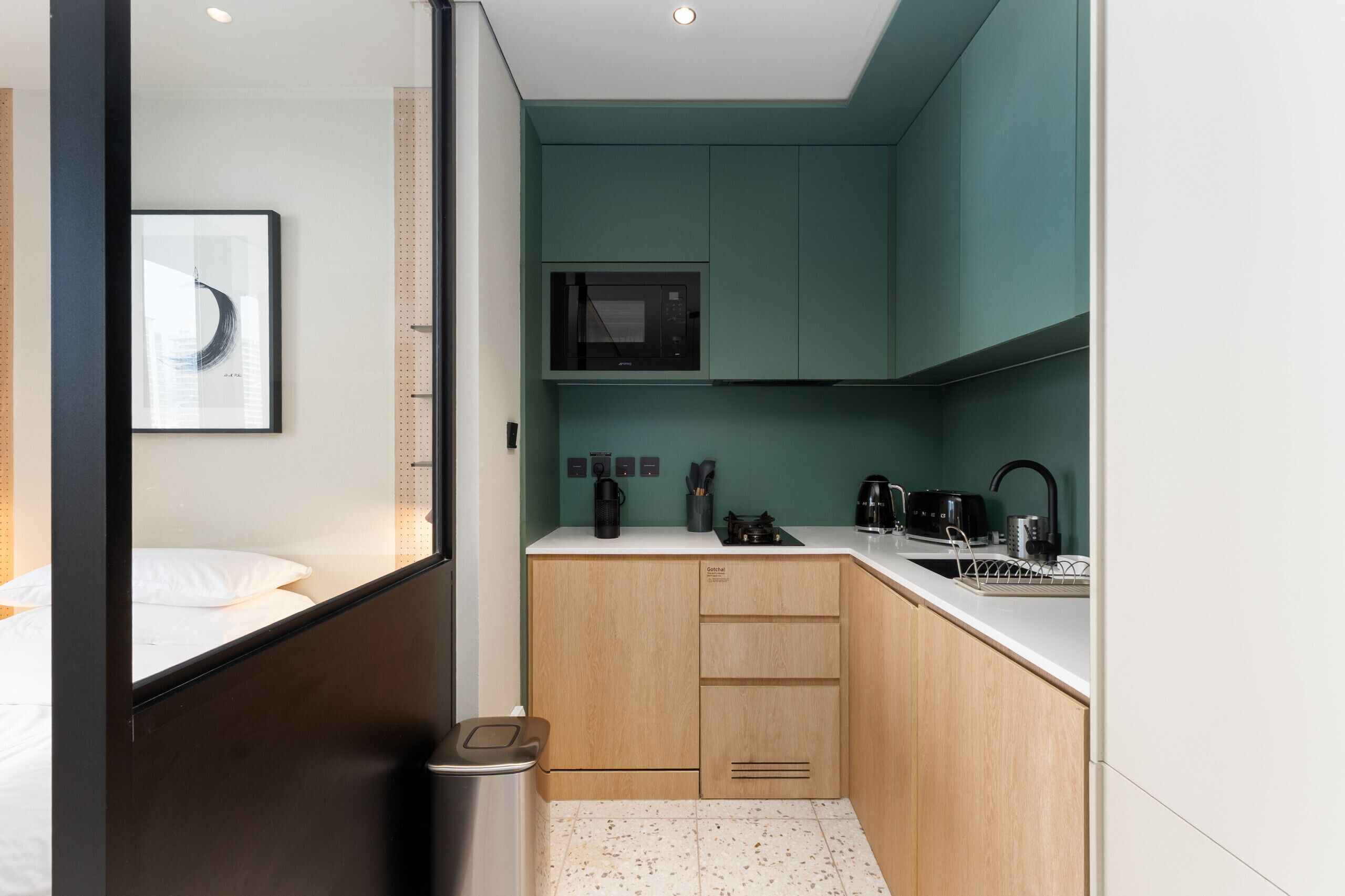 Een compacte hotelkamer met een bed, een klein kitchenette, een magnetron, een waterkoker, een broodrooster en een prullenbak.