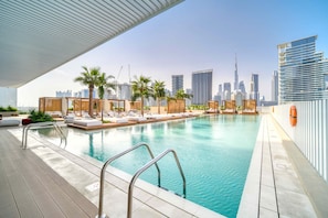 A rooftop pool with lounge areas, palm trees, and a city skyline in the background. - Sleek Studio w/ Burj Khalifa View (Dubai)