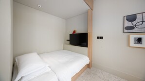 Ein Schlafzimmer mit einem Einzelbett, einem Fernseher auf einem Regal und einem gerahmten Bild an der Wand.