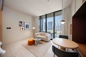 A modern hotel room with a large window offering a city view, a sofa, a small round table, and a dining table with chairs. - Modern Studio Near Downtown | Burj View (Dubai)