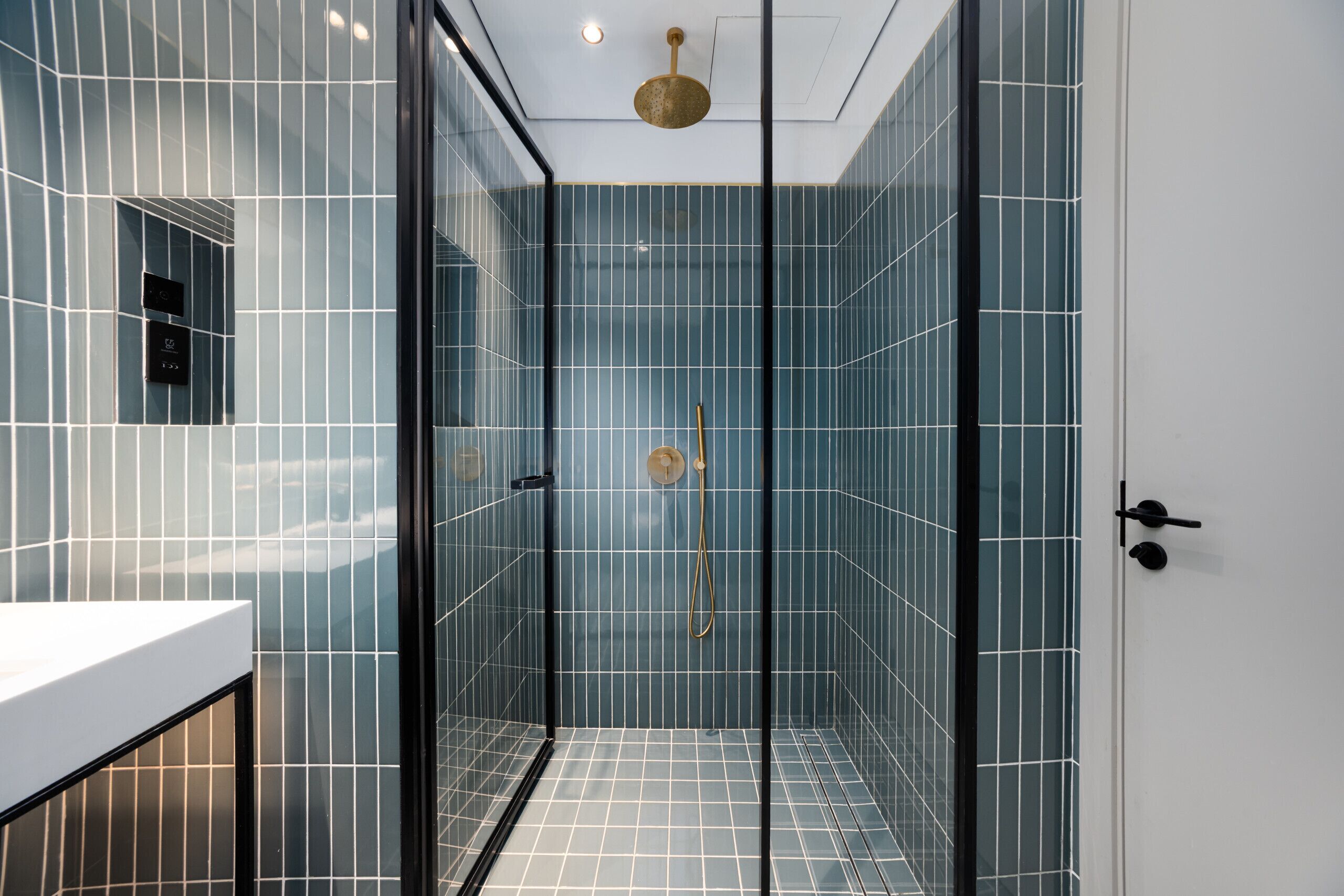 Ein modernes Badezimmer mit Duschkabine aus Glas, einer weißen Ablagefläche und einer sichtbaren Bedienkonsole.