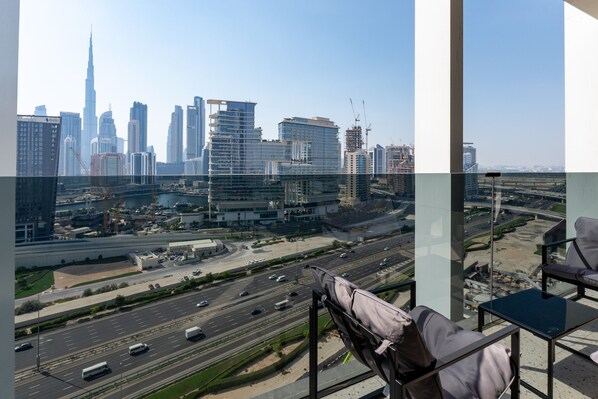 A high-rise hotel room with a city skyline view, a balcony with a chair, and a dining area. - Chic City Studio in Upside w/ Burj View (Dubai)