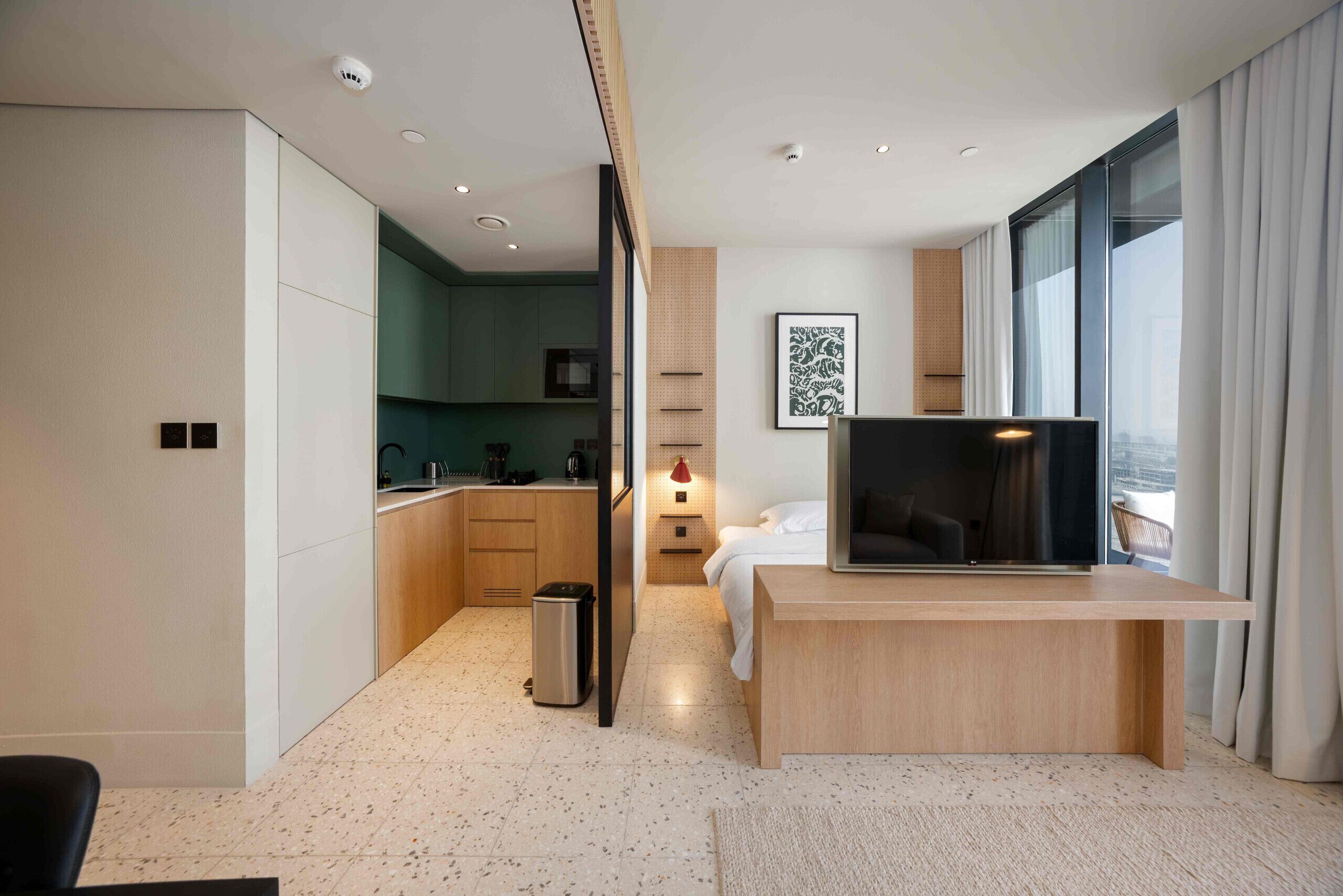 Een moderne hotelkamer met een kitchenette, een bed, een televisie en een groot raam.