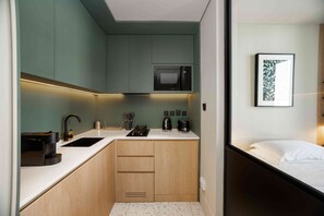 A compact kitchen with a microwave, sink, and wooden cabinets. - Furnished Business Bay Studio w/ Balcony (Dubai)