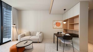 A modern living room with a sofa, a round coffee table, a dining table with chairs, and a bookshelf. - Furnished Business Bay Studio w/ Balcony (Dubai)
