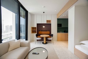 A modern hotel room with a sofa, a round table, a dining area, and a view of the cityscape. - Relaxed Studio in Upside w/ Burj View (Dubai)