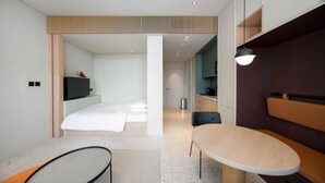 Quarto de hotel moderno com uma cama, uma escrivaninha, uma cadeira e uma pequena mesa.