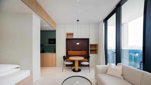 A modern hotel room with a sofa, a round table, a kitchenette, and a city view. - Contemporary Studio w/ Burj View (Dubai)