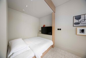 Ein Schlafzimmer mit einem Bett, einem angebrachten Fernseher und einem gerahmten Bild an der Wand.