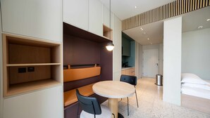 A modern hotel room with a round table, two chairs, a bench, and a bed. - Sleek Business Bay Studio | Burj View (Dubai)
