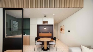 Um interior moderno com área de refeições, incluindo mesa redonda e cadeiras, cozinha com divisória de vidro e sala de estar com sofá e uma pintura na parede.