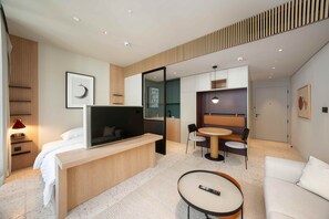 Ein modernes Hotelzimmer mit einem Bett, einem Fernseher, einem Schreibtisch, einem Essbereich und einem Sofa.