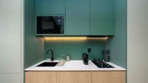 A modern kitchen with a white countertop, a black faucet, a stainless steel sink, a black microwave, a coffee maker, and a gas stove. - Modern Upside Studio w/ Skyline View (Dubai)
