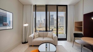 A modern hotel room with a sofa, a small round table, a chair, and a view of a cityscape through large windows. - Modern Upside Studio w/ Skyline View (Dubai)
