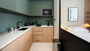 Een compacte kitchenette met een magnetron, waterkoker en koffiezetapparaat, een klein spoelgedeelte en een prullenbak.