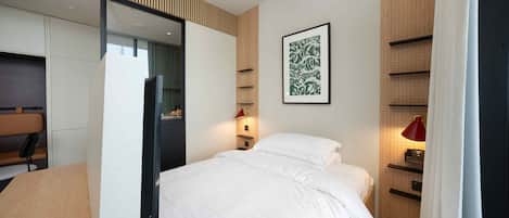 Ein modernes Hotelzimmer mit einem Bett, einem Schreibtisch, einem Sessel, einem Kleiderschrank und einem an der Wand befestigten Regal.