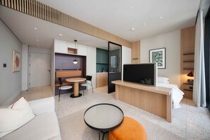 Una habitación de hotel moderna con cama, televisión, zona de estar con mesa y sillas, kitchenette y baño.