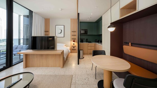 Quarto de hotel moderno com uma cama, TV, área de refeições e cozinha.