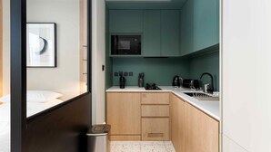 Quarto de hotel compacto com cozinha compacta, uma cama, um cesto de lixo e um quadro na parede.