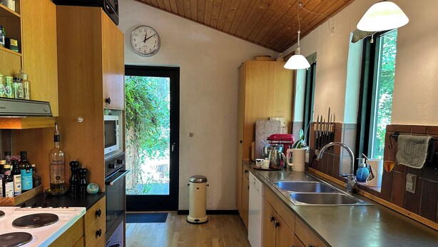 Une cuisine avec des meubles en bois, un évier en acier inoxydable et une horloge au mur.