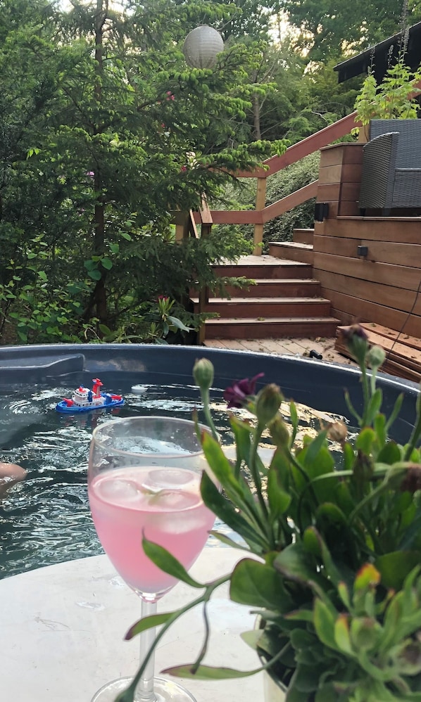A hot tub with a toy boat, surrounded by greenery and a wooden deck.
