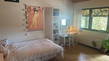 A bedroom with a bed, a desk with a chair, a vanity with a mirror, and a window with curtains.