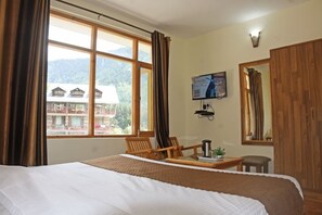 Une chambre d’hôtel avec un lit, un bureau avec une cafetière, une chaise, une télévision et une fenêtre avec des rideaux.