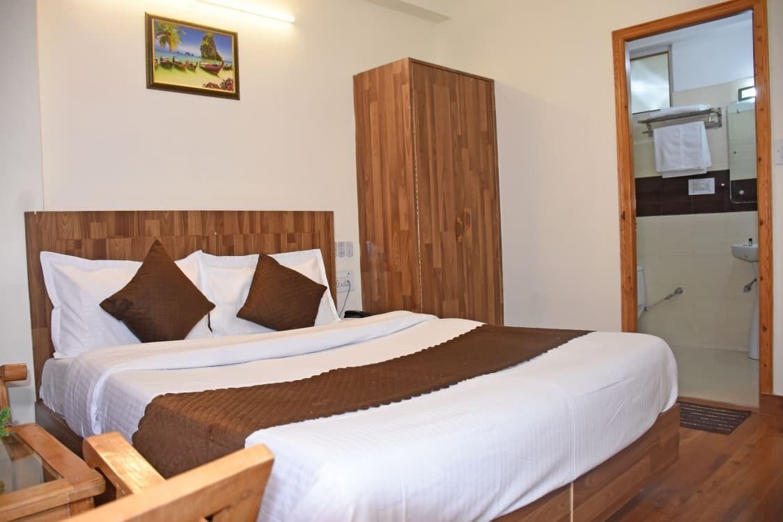 A bedroom with a wooden headboard, a bed with white and brown bedding, a wardrobe, and a bathroom with a shower.