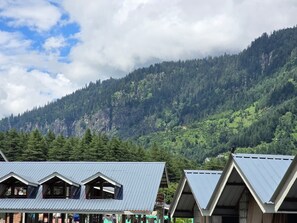 A row of cabins with pitched roofs, set against a backdrop of a forested mountain.