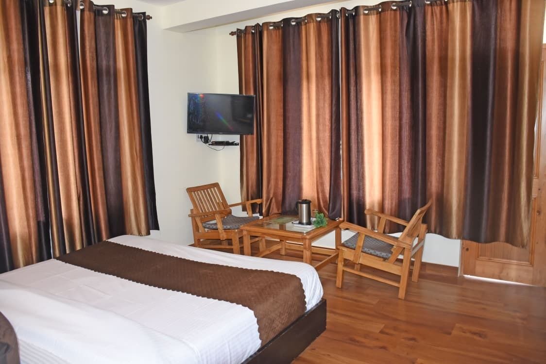 A hotel room with a bed, a TV mounted on the wall, and two wooden chairs with a table.