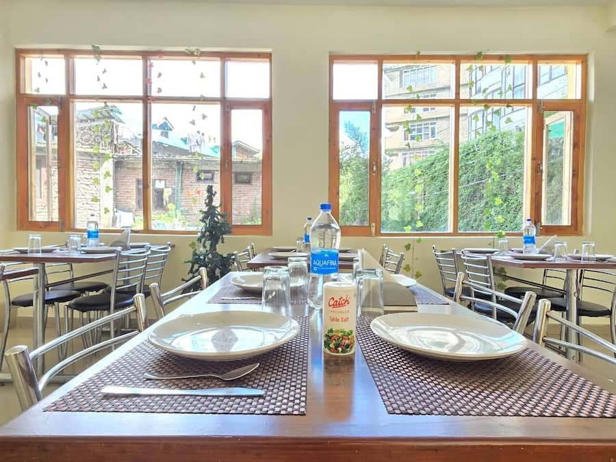 Comedor con mesas dispuestas para dos, con platos, cubiertos y vasos.