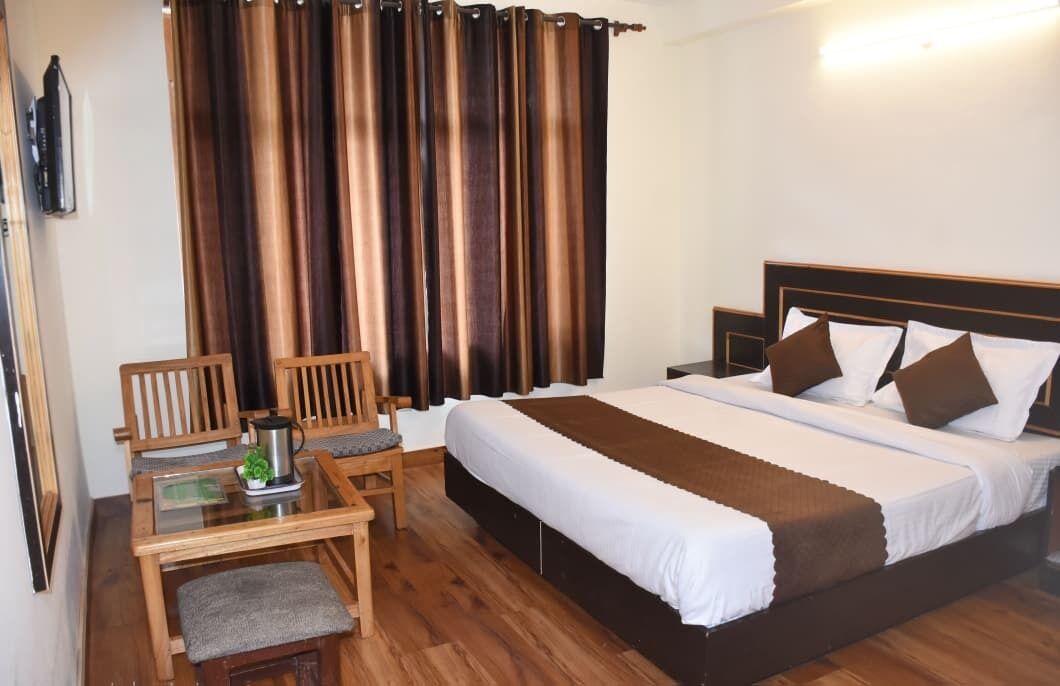 A hotel room with a bed, a desk with a chair, and a large window with curtains.
