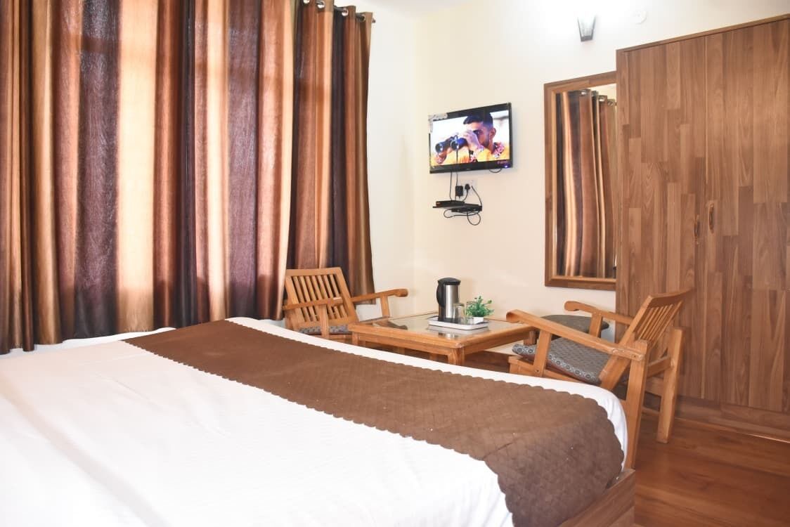 Habitación de hotel con una cama, dos sillas de madera, una mesita con cafetera, un televisor montado en la pared y un armario.