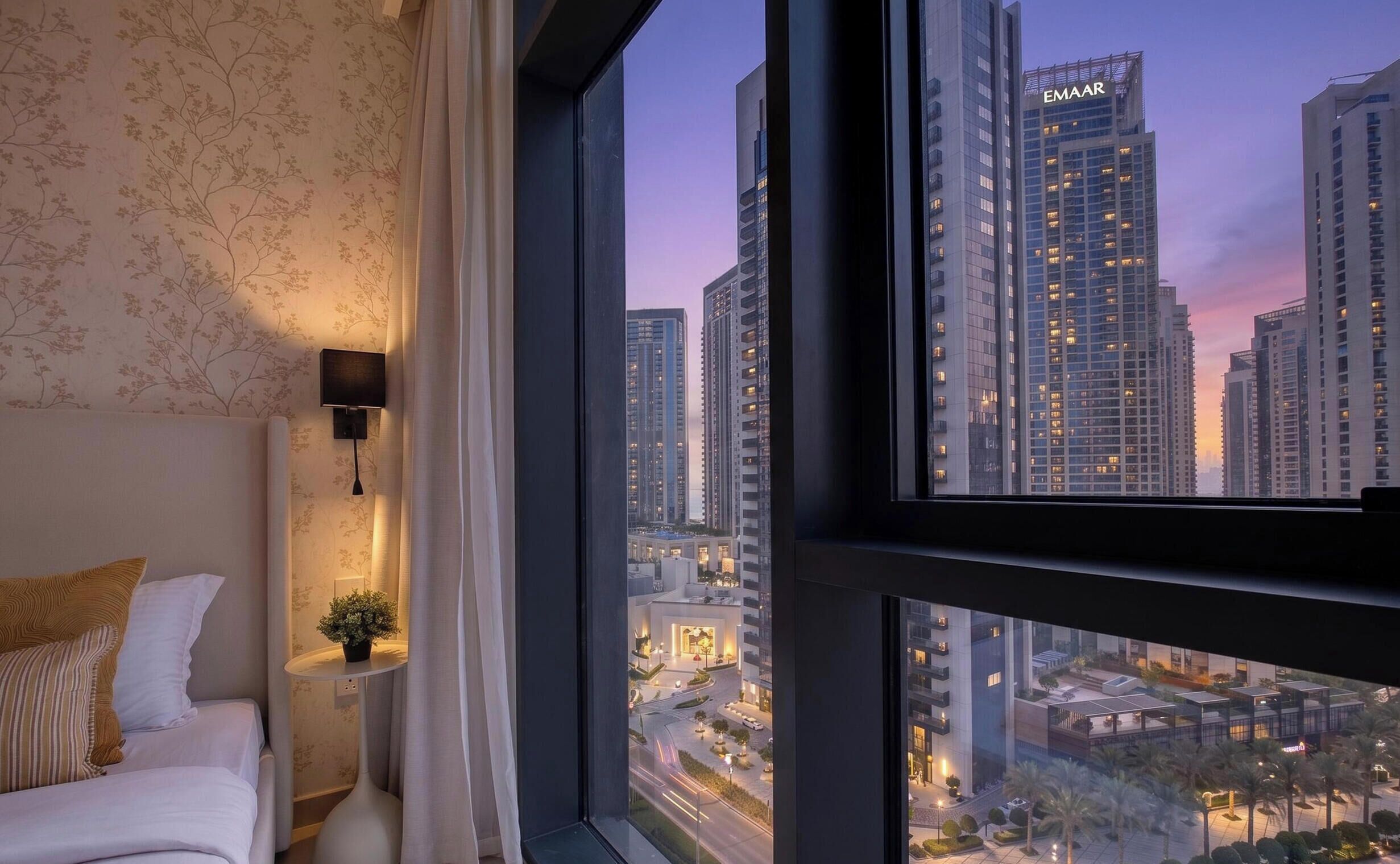 Une chambre d’hôtel avec une grande fenêtre, un lit, une table de chevet et une vue sur un paysage urbain avec de hauts immeubles.