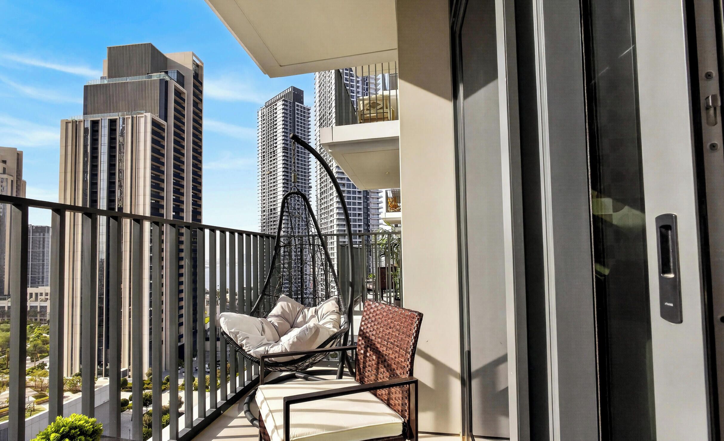 A balcony with a chair and a hanging chair, overlooking a cityscape with tall buildings.