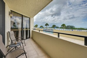 A balcony with a view of a beach, a table with chairs, and a window with curtains. - Pool, Pickleball & Beach! Gulf Island Club Condo (Hudson)