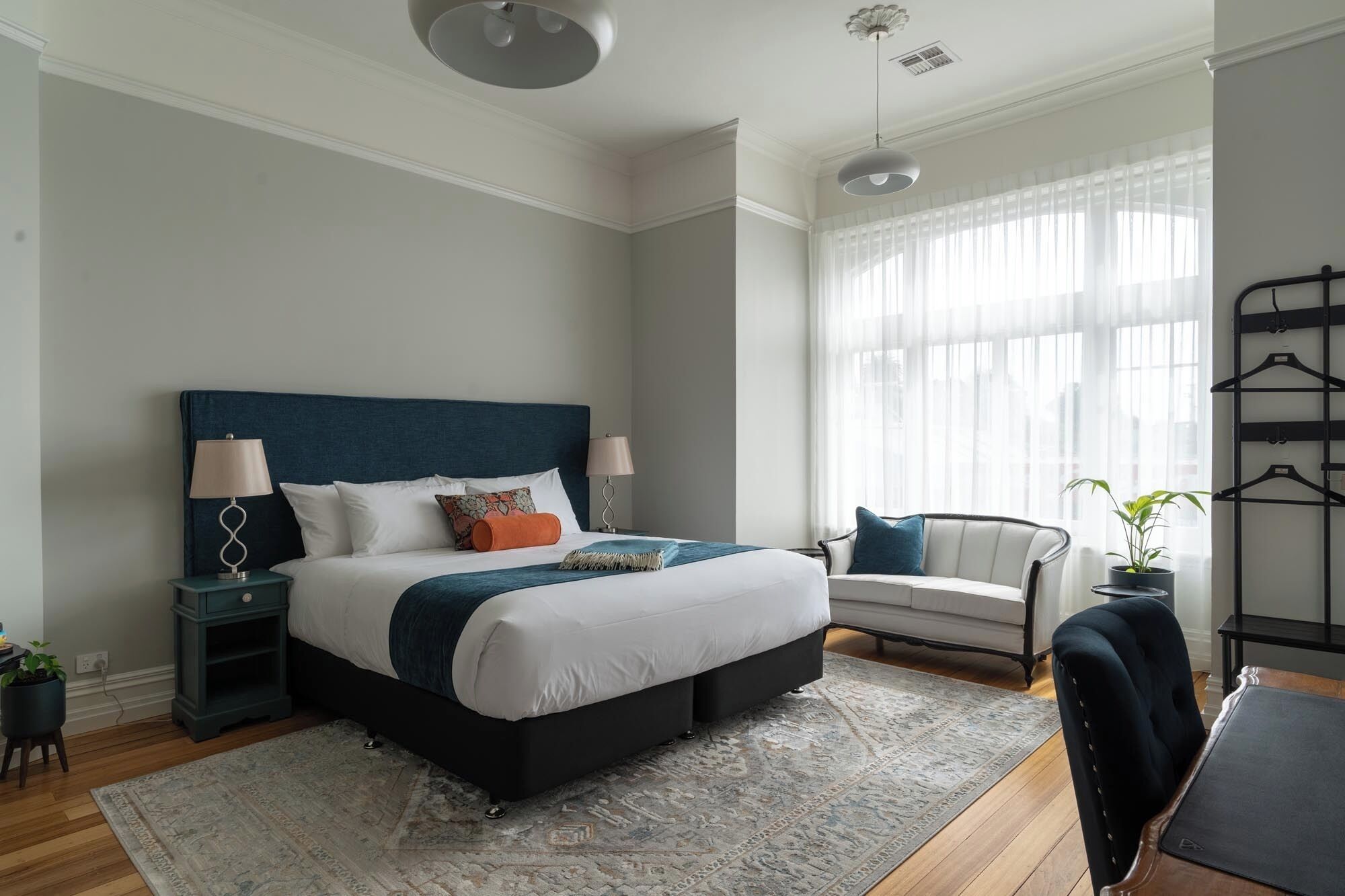 Un dormitorio moderno con una cama grande, mesitas de noche, una silla, un escritorio y una ventana con cortinas de gasa.