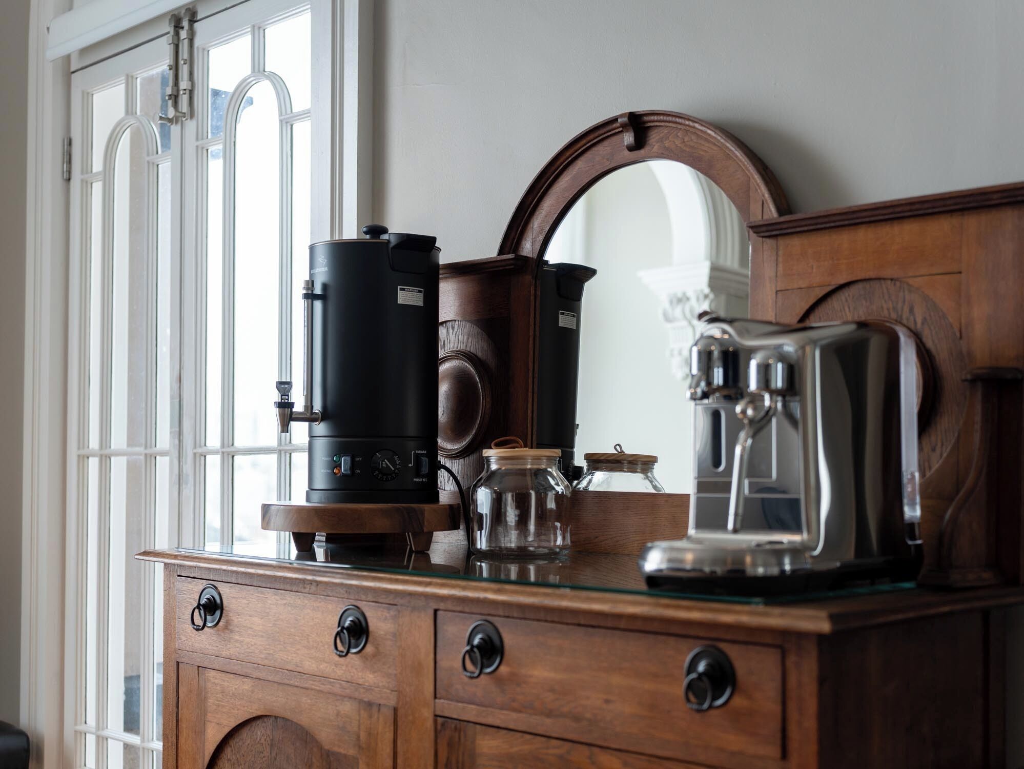 A wooden dresser with drawers, a coffee maker, a glass jar, and a mirror.