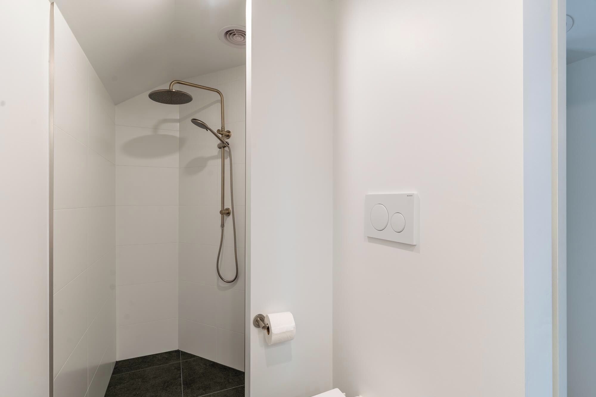 A shower with a handheld showerhead and a wall-mounted control panel.