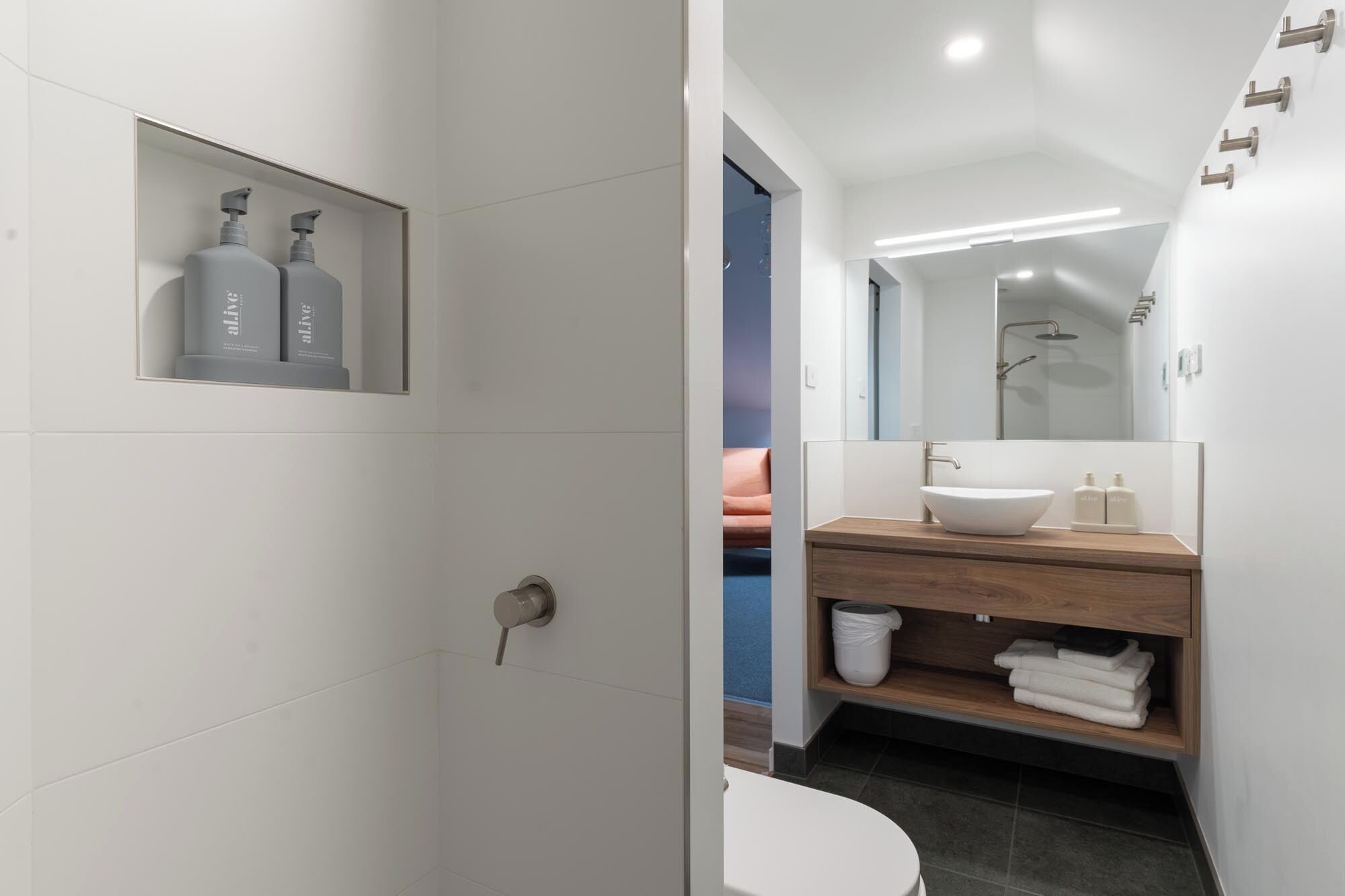 Un baño moderno con lavamanos blanco, tocador de madera y zona de ducha.
