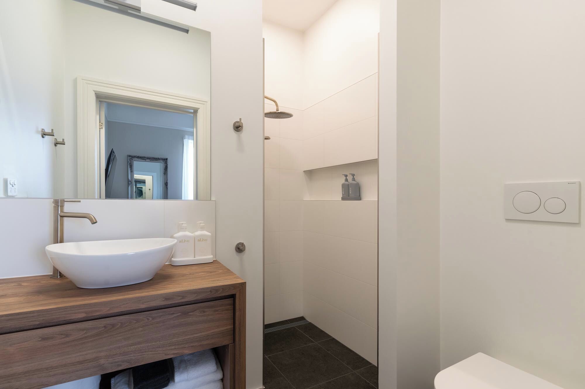 A modern bathroom with a white sink, wooden vanity, a mirror, a shower, and a toilet.