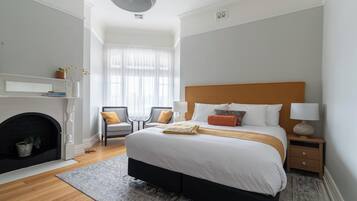 Un dormitorio con una cama, dos sillones, una chimenea y una mesita de noche.